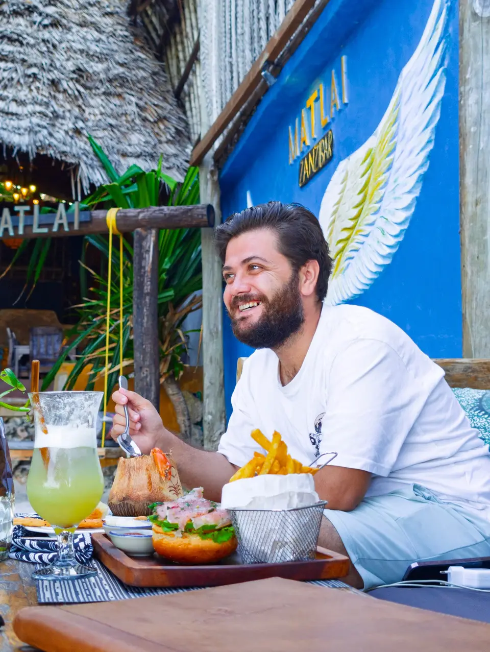 Guest sitting on a dhow lounger at the beachfront of Boutique Hotel Matlai Zanzibar, enjoying a mocktail and food.