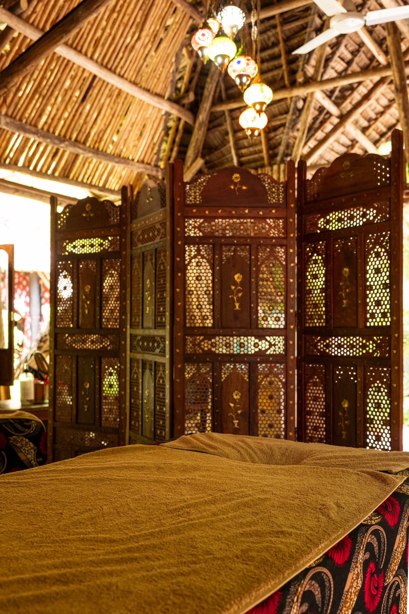 A massage bed at Bustani behind a carved screen, lit by coloured lanterns.